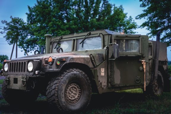 Military green Humvee parked outdoors surrounded by trees.