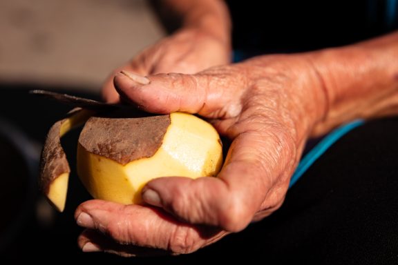 A person's hands holding a partially peeled yellow fruit.